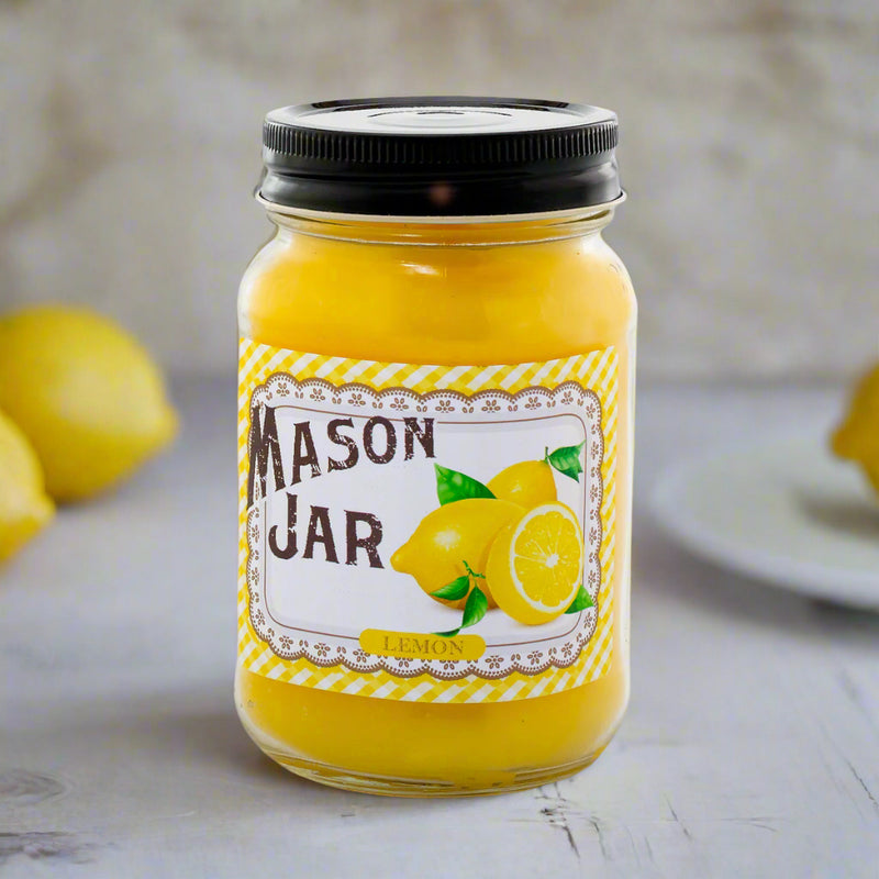 A Mason jar candle with a yellow label featuring lemon illustrations. The candle is placed on a surface with lemons and a white plate in the background.