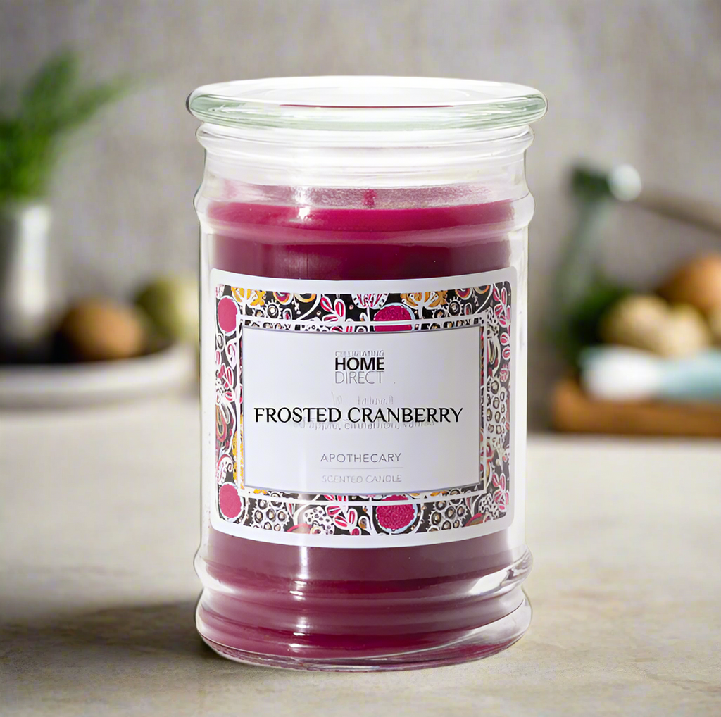 A frosted cranberry scented Apothecary candle in a clear glass jar with a decorative label, sitting on a kitchen counter.