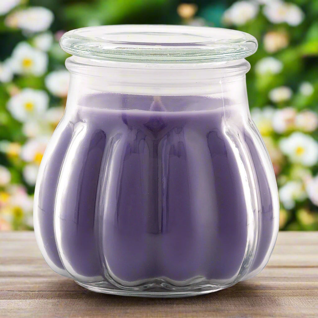 A purple Contempo candle in a clear glass jar, set on a wooden surface with a floral background.