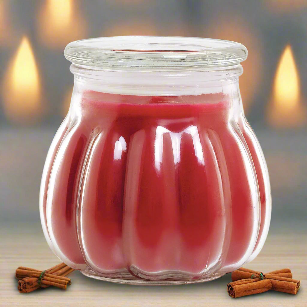 A red Contempo christmas candle in a clear glass jar with a lid, accompanied by cinnamon sticks.