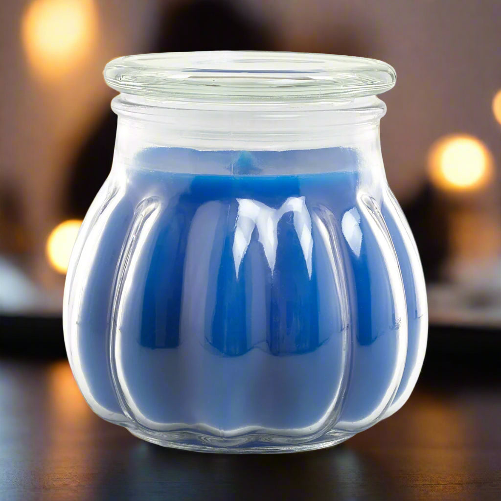 blue candle contained within a clear glass jar with a textured design, set on a table with blurred lights in the background.