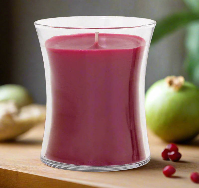 red candle in a clear elegant glass holder with pomegranate seeds and fruit on a brown background