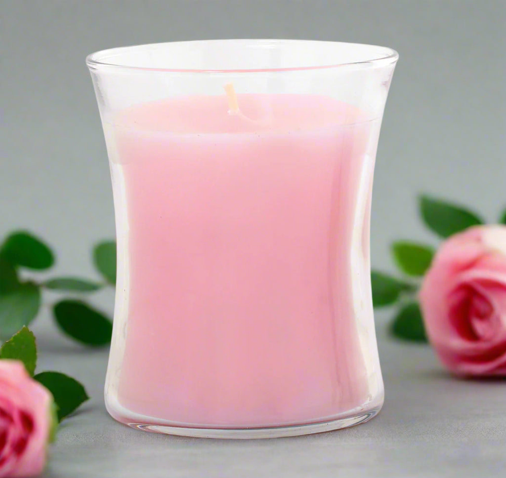 Pink candle in a clear elegant glass container on a white background with roses