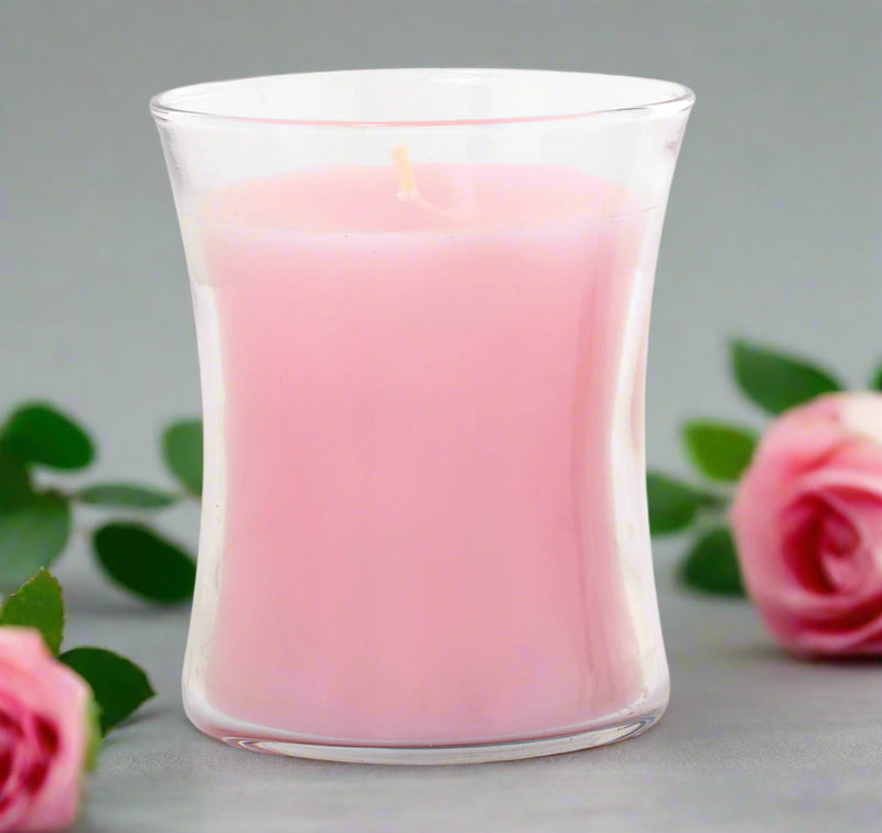 Pink candle in a clear elegant glass container on a white background with roses