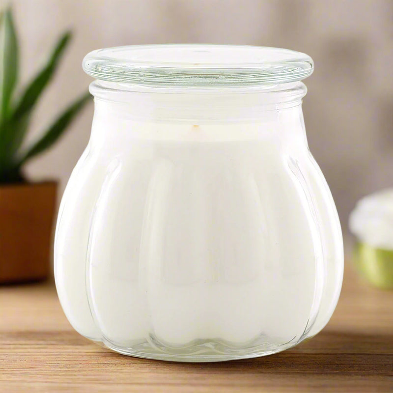 A white Contempo candle in a clear glass jar, with lid. sitting on a table