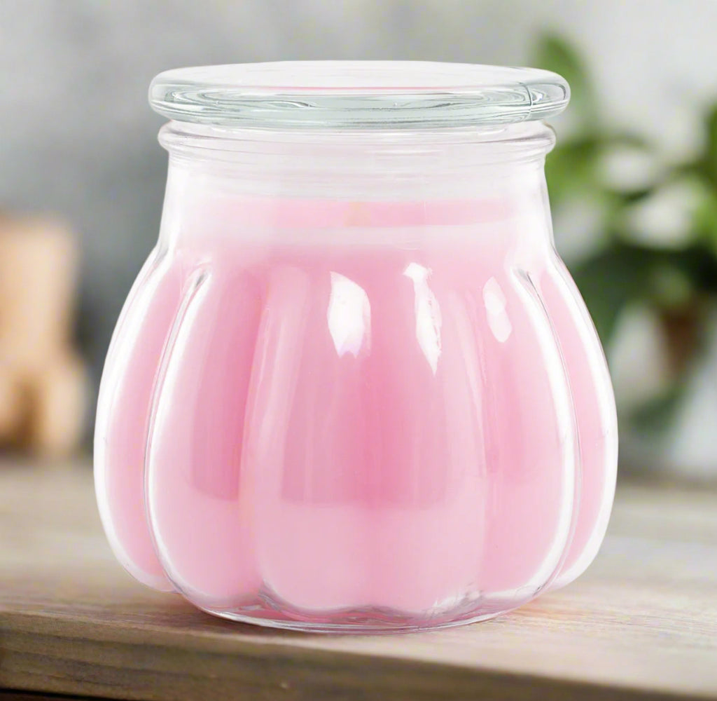 A pink candle contained within a clear glass jar.